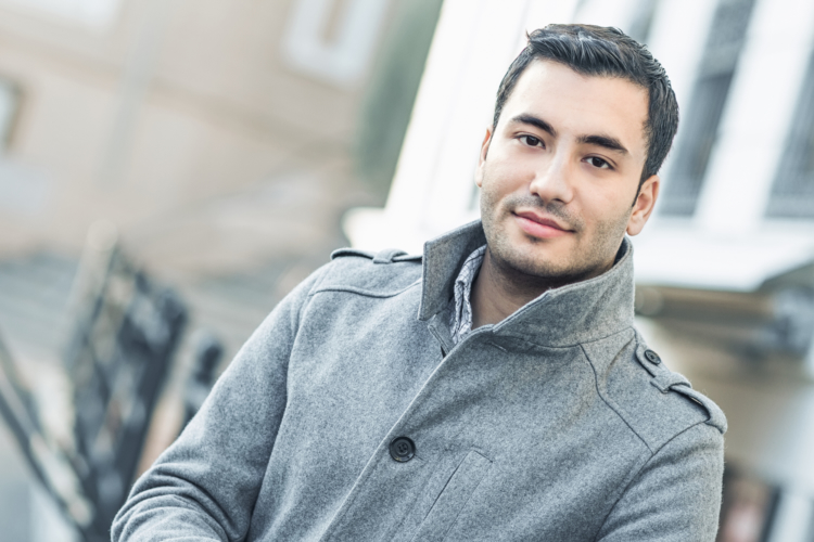 A confident male candidate wearing a stylish grey coat smiling before attending a professional job interview.