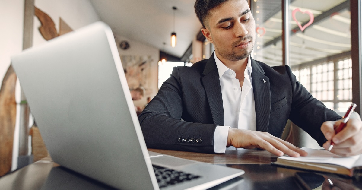 A candidate taking notes in a notepad next to a laptop while preparing for a job interview.