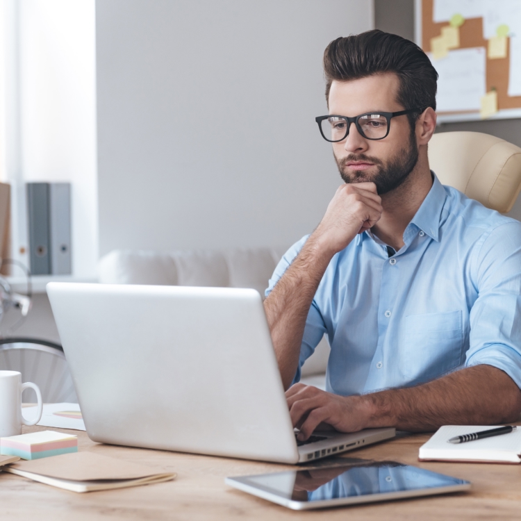 A thoughtful job seeker sitting at a desk reviewing job specifications and auditing transferable skills on a laptop.
