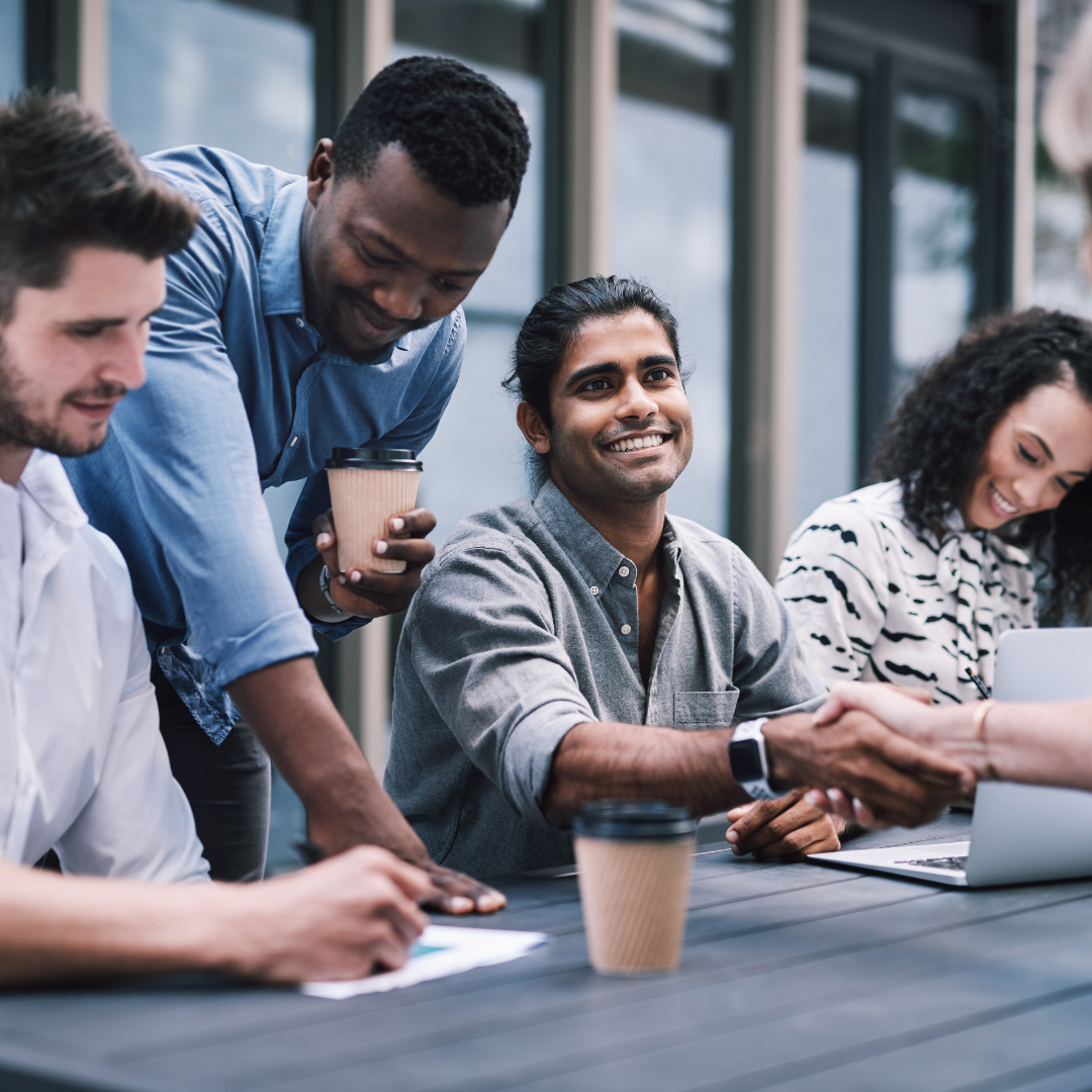 A group of people sitting on a table outside with some laptops introducing each other in a networking event. This is part of proactive recruitment.