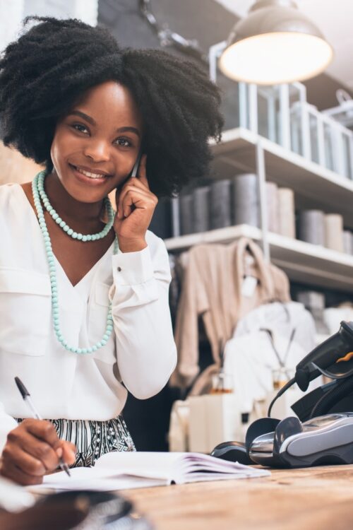 A retail specialist taking customer notes on the phone behind a counter, highlighting candidate potential when transitioning from retail to sales.