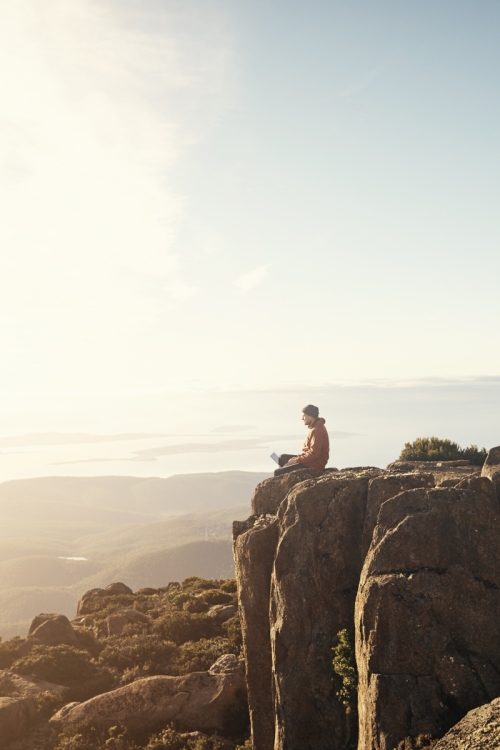 A professional seated on a mountain ledge looking out toward the horizon, illustrating long-term career vision and autonomy to attract top sales professionals.