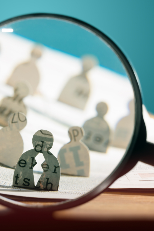 A magnifying glass focusing on candidate cut-outs, representing how to attract top sales professionals beyond standard salaries.