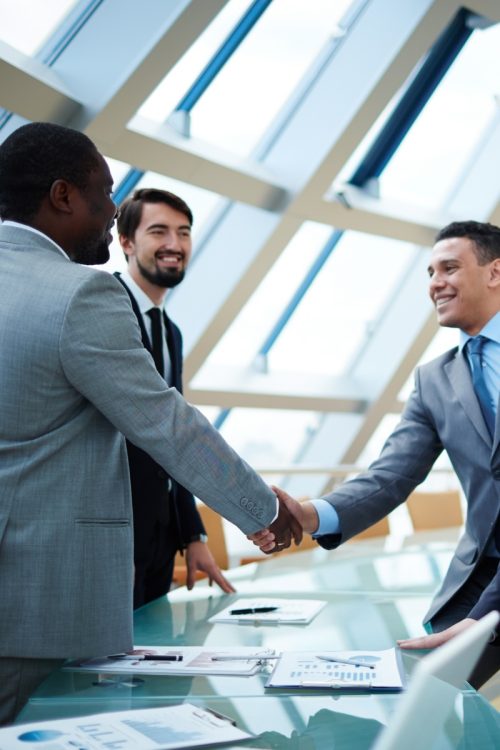 Business executives shaking hands across a boardroom table, representing Mark's transition from military to sales leadership.