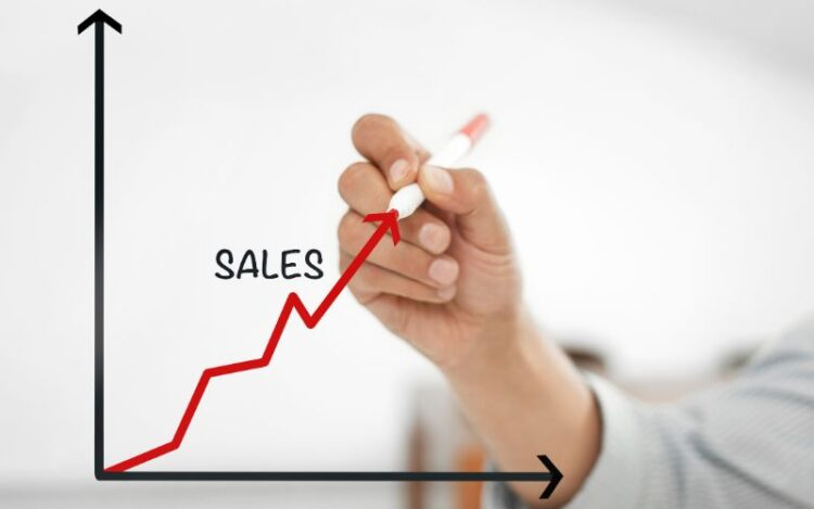 A hand drawing an upward-trending red line graph labeled sales, representing performance growth and self-motivation in sales.