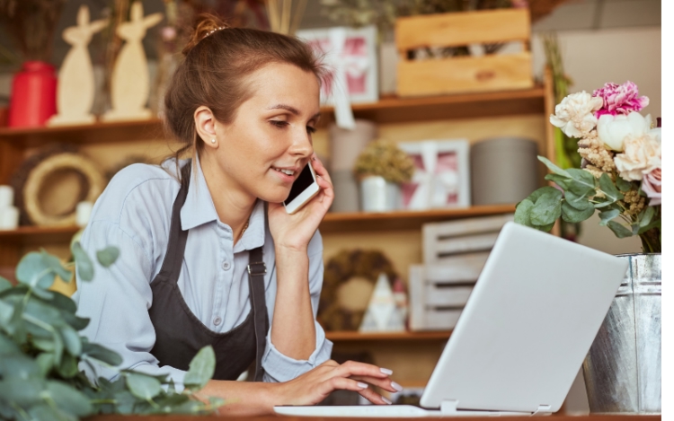 A self-employed sales consultant managing client phone calls and pipeline data on a laptop, illustrating managing a self-employed sales team.