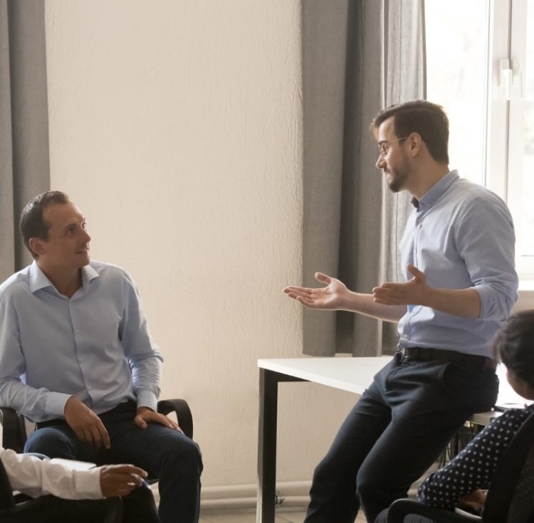 A sales manager leading an open team discussion with colleagues in a bright office, illustrating sales staff retention through strong core values.