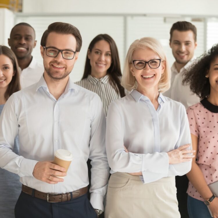 A diverse group of smiling sales professionals standing together in a bright modern office workspace.