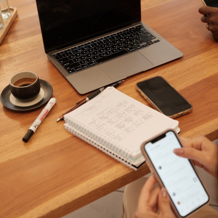 A collaborative workspace setup with a laptop, smartphone, coffee, and handwritten strategy notes on a wooden desk.