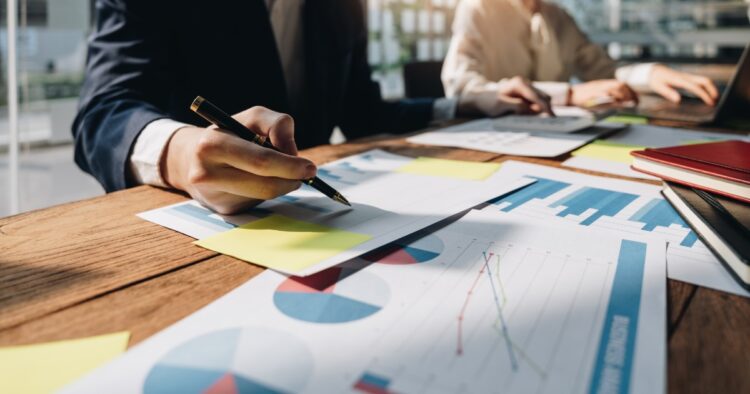 A business professional reviewing printed charts, graphs, and performance strategy reports at an office desk.