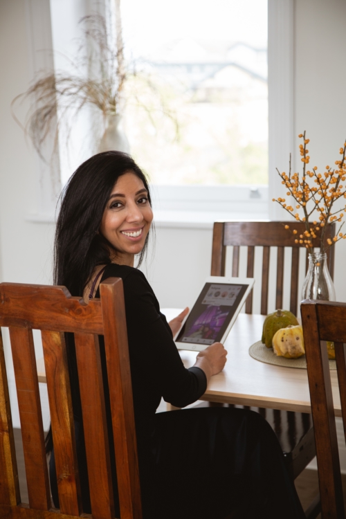 Citrus Connect Founder Leena Parmar sitting at a wooden table smiling while holding a tablet.