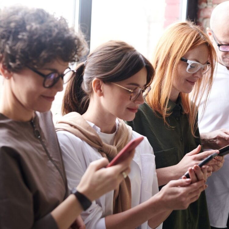 A row of colleagues from varying age demographics reviewing mobile technology and digital devices in an office.