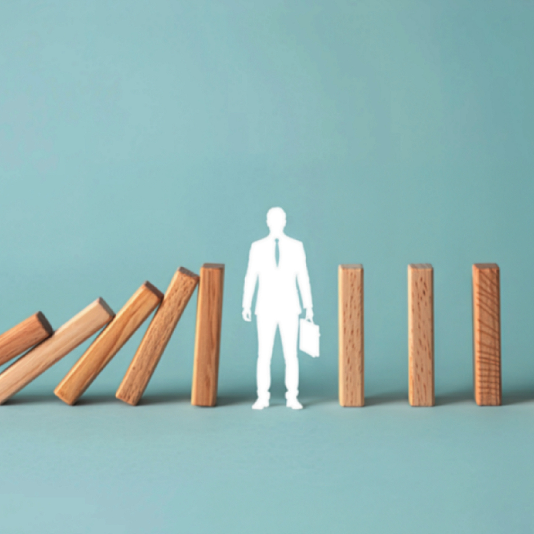 White cutout figure of a business professional stopping falling wooden dominos, representing resilience and pipeline momentum.
