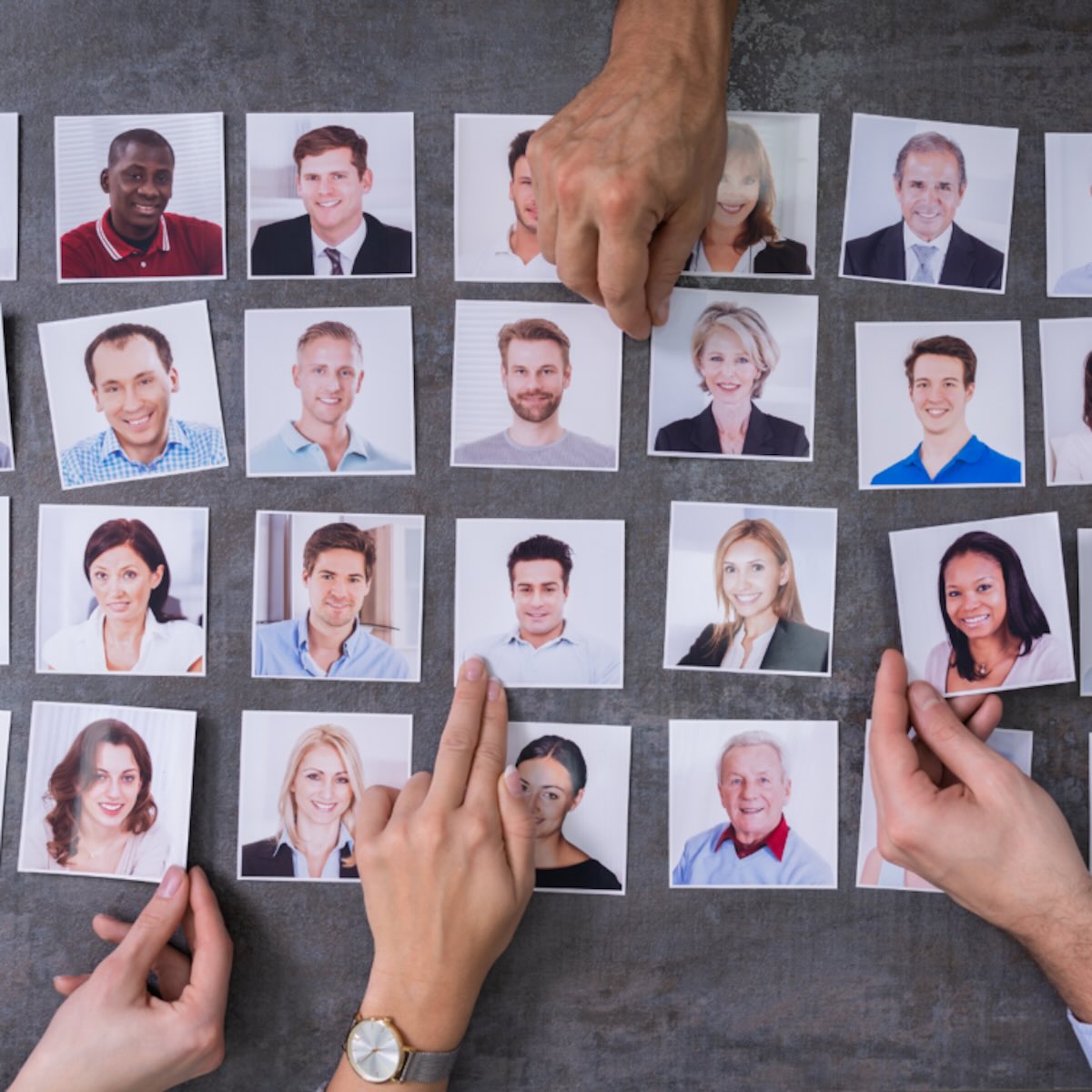 Hands selecting candidate headshots during a thorough sales recruitment strategy vetting process.