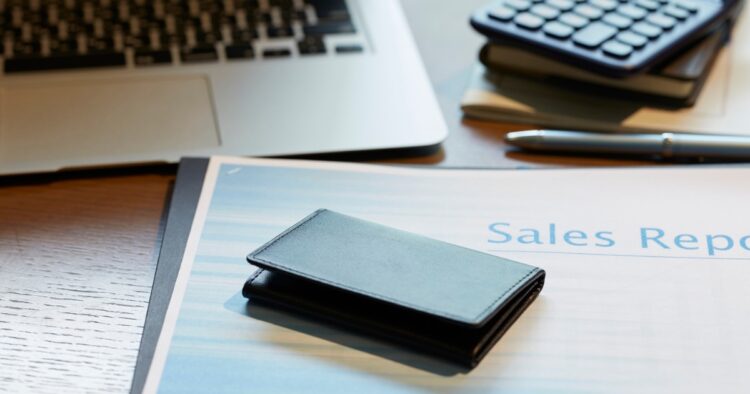A professional desk setup featuring a laptop, calculator, and sales report document for a flexible sales role.