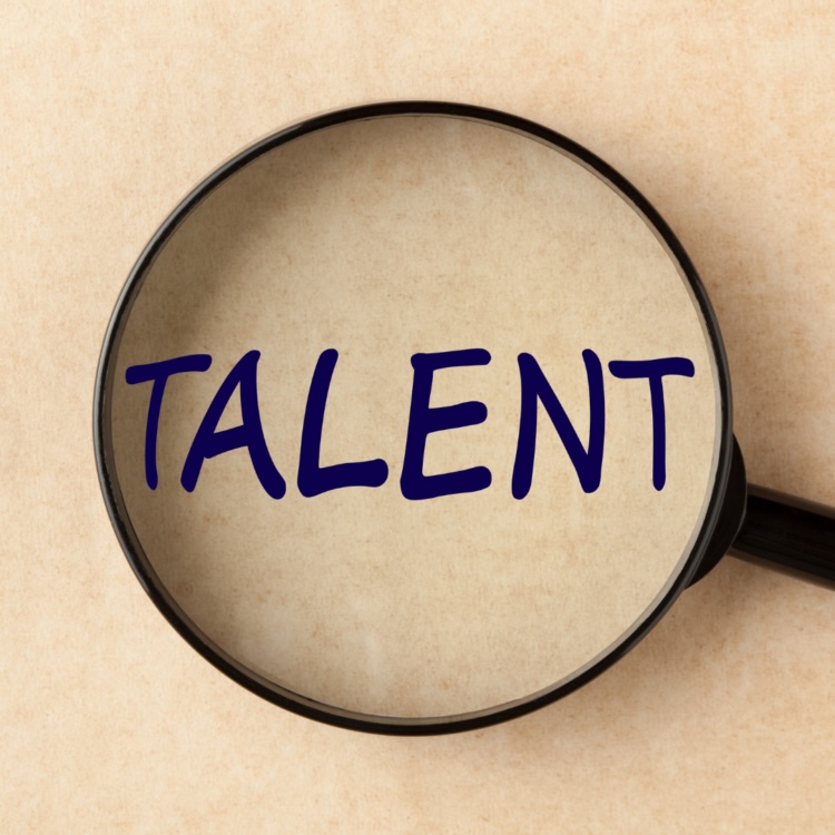 A magnifying glass focusing on the word TALENT, representing proactive talent sourcing in direct sales.