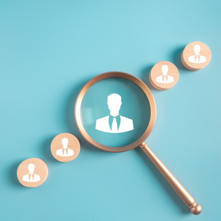 A magnifying glass focusing on candidate icons to find top talent for sales recruitment.