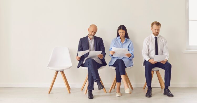 Three job applicants sitting in a waiting room reviewing their CVs before an interview.