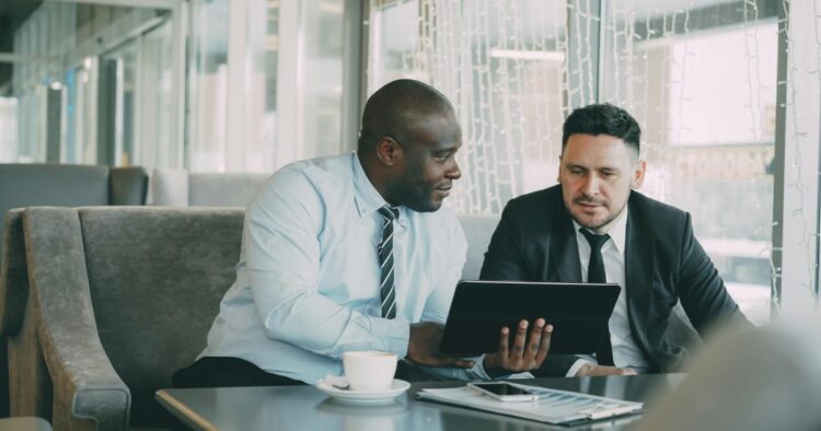 Two business professionals reviewing sales recruitment strategies on a tablet during a consultation meeting.